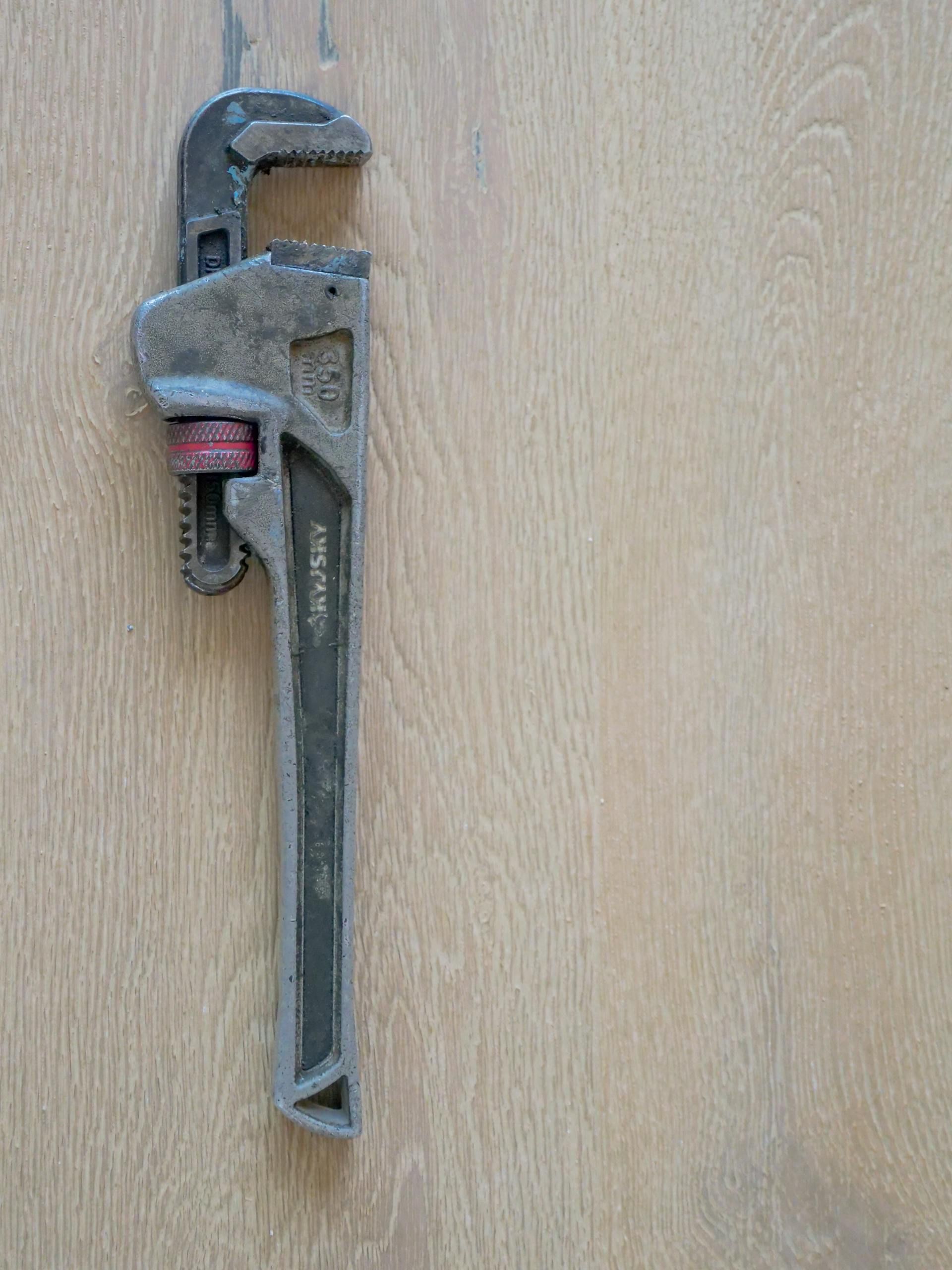 Close-up of a metal plumber's wrench against a wooden surface, showcasing tool detail. Close-up of a metal plumber's wrench against a wooden surface, showcasing tool detail.